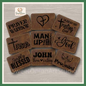 May include: A collection of eight rectangular brown faux leather patches with stitched edges, each featuring black laser-engraved religious text and symbols including phrases like Prayer Warrior, Man Up, Jesus, and Child of God.