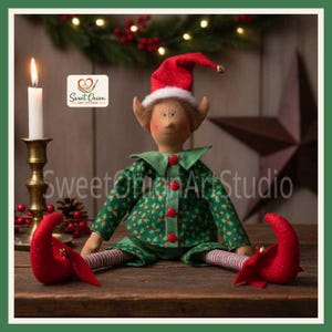 May include: A fabric elf doll wearing a green shirt and pants with a holly leaf pattern, red buttons, and a red hat with a white trim. The doll has striped legs and red curled shoes with small bells. The text Sweet Onion Art Studio is visible.