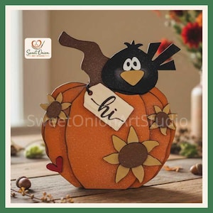 May include: A decorative orange pumpkin cutout featuring a black crow perched on top, three yellow sunflowers, a small red heart, and a beige tag hanging from the stem with the word hi written in black script. The surface has a glittery texture.