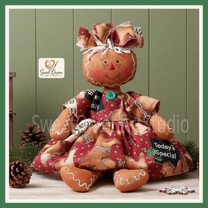May include: A fabric gingerbread doll with a round brown head, stitched facial features, and a red bow on top. The doll wears a red dress patterned with gingerbread cookies, green dots, and black chalkboard-style labels reading Today's Special.