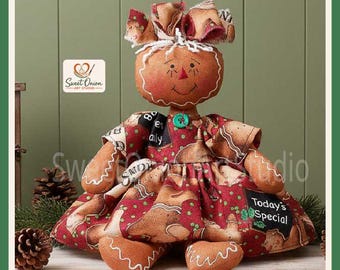 May include: A fabric gingerbread doll with a round brown head, stitched facial features, and a red bow on top. The doll wears a red dress patterned with gingerbread cookies, green dots, and black chalkboard-style labels reading Today's Special.