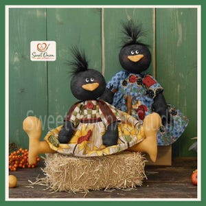 Könnte beinhalten: Zwei schwarze Stoffpuppen mit buschigem Haar und orangefarbenen Schnäbeln. Die vordere Puppe trägt ein grün-weiß kariertes Oberteil mit einem gelben Sonnenblumenrock. Die hintere Puppe trägt ein blaues Blumenkleid. Ein Logo zeigt Sweet Onion Art Studio.