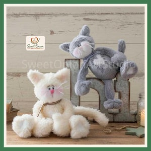 May include: Two plush cat toys, one cream-colored and one gray, featuring soft fur, stitched facial details, pink noses, and long whiskers. The gray cat is positioned atop a large, weathered metal letter N, while the cream cat sits below.