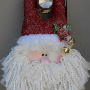 以下が含まれることがあります： 赤いフェルトのサンタクロースのドアハンガーで、白いひげ、ピンクの顔、黒い目があります。サンタは帽子に白いファーのトリムと、赤い実のついた緑のホーリーの枝が付いています。ホーリーの枝には金色のベルが2つぶら下がっています。