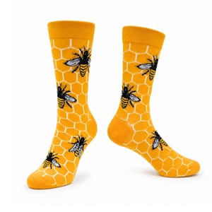 May include: A pair of crew-length socks featuring a vibrant yellow background with a white hexagonal honeycomb pattern and multiple black and yellow bee illustrations scattered across the fabric, including the toe, heel, and leg sections.