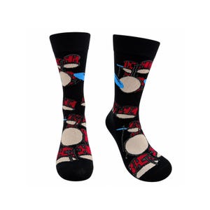 May include: A pair of black crew socks featuring a repeating pattern of red drum kits with beige drum heads and light blue cymbals. The socks have a solid black ribbed cuff at the top and a black heel and toe section, showcasing a musical theme.