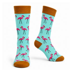 Könnte beinhalten: Ein Paar Socken mit hellblauem Hintergrund und einem sich wiederholenden Muster aus leuchtend rosa Flamingos. Die Socken haben ein einfarbig braunes Rippbündchen am oberen Rand und eine braune Zehenpartie, die einen Kontrast zum hellblauen Stoff bildet.