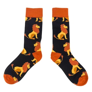 May include: A pair of black socks featuring a repeating pattern of cartoon lions in yellow and orange. The socks have orange heels and cuffs. The socks are designed for adults.