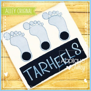 Puede incluir: Tres huellas de pies de bebé azules con contorno negro y una pancarta negra con el texto "Tarheels" en blanco con contorno azul.