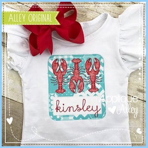 May include: A white t-shirt with a blue and white patterned square featuring three red embroidered lobsters. The square also includes the name "kinsley" in white text.