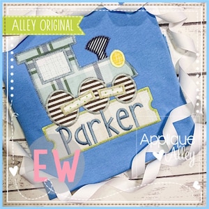 May include: A blue t-shirt with a personalized applique of a train with wheels and a sign that says "Parker". The applique is made of different patterned fabrics in shades of blue, brown, and green.