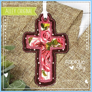 May include: A brown and pink cross with a floral design. The cross is decorated with white polka dots and has a loop at the top for hanging.