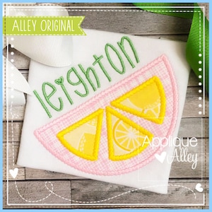 May include: A white shirt with the name Leighton embroidered in green thread. A pink and yellow lemon slice applique is stitched on the shirt.