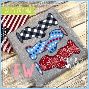 May include: A gray t-shirt with three decorative appliques in patriotic patterns: a black and white checkered design, a blue star pattern, and a red firework design. The text "EW" is in pink.