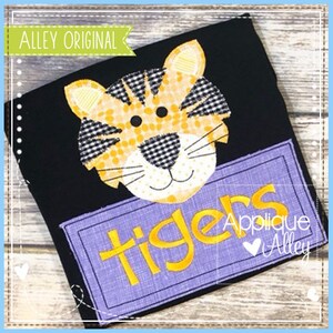 Puede incluir: Una camiseta negra con una aplicación de tigre en amarillo y morado, con la palabra "Tigers" y el texto "Applique Alley" debajo.