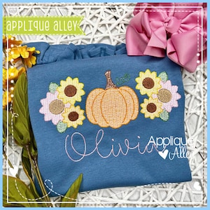 Puede incluir: Una camisa azul con una calabaza y girasoles bordados. El nombre "Olivia" está bordado debajo de la calabaza y los girasoles. La camisa está sobre una superficie de mimbre blanca.