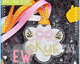 May include: A personalized Halloween ornament with the name "Skye" embroidered in gold. The ornament features a cloud shape, a pink bow, and two jack-o'-lanterns. It is adorned with orange and pink ribbons and the text "applique alley".