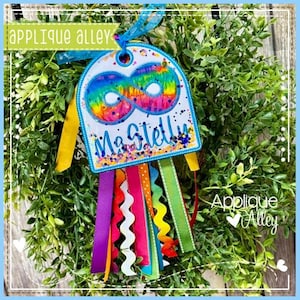 Può includere: Un'etichetta personalizzata a forma di simbolo dell'infinito arcobaleno con il nome "MaStelly" in corsivo blu. L'etichetta è adornata da nastri colorati e dal testo "Applique Alley".