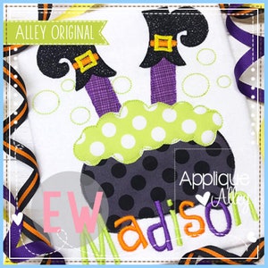 Pode incluir: Design de aplique de pernas de bruxa saindo de um caldeirão com bolinhas verdes e brancas. O caldeirão está borbulhando e as pernas da bruxa são roxas com botas pretas. O design está em um tecido branco com o texto "Applique Alley" e "Madison" em fio laranja.