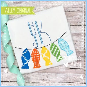 May include: A white t-shirt with a monogram of the letters "HK" in blue thread. Below the monogram is a string of five colorful fish-shaped ornaments.