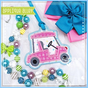 May include: Pink and white golf cart applique with a polka dot pattern. The applique is surrounded by a blue outline and has a white background.