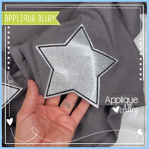 May include: A silver glitter star applique with a black outline on a gray fabric background. The text "Applique Alley" is visible in the bottom right corner of the image.
