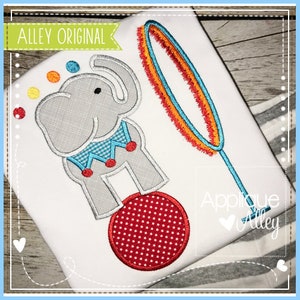 May include: Embroidered design of a gray elephant balancing on a red ball with a blue and orange hoop in the background. The design is stitched on a white t-shirt. "Alley Original" and "Applique Alley" are stitched on the shirt.