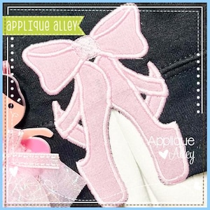 May include: Pink felt applique of a pair of ballet shoes with a bow on top. The applique is on a black fabric background. The text "Applique Alley" is visible in the bottom right corner.