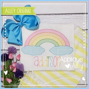 May include: A white shirt with a rainbow and clouds embroidered on it. The name "Addison" is embroidered below the rainbow. The text "Applique Alley" is embroidered in the bottom right corner.