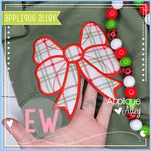 May include: A red and white plaid bow applique with a green outline. The applique is on a green fabric background. The text "Applique Alley" is visible in the bottom right corner of the image.