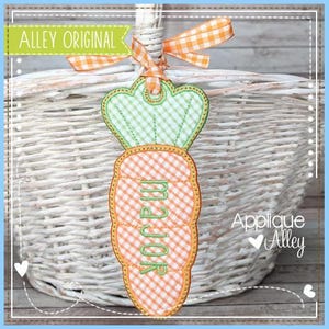 May include: A carrot-shaped applique with the word "major" embroidered in green thread. The carrot has a green and white checkered top and an orange and white checkered body. The applique is hanging from a white wicker basket.