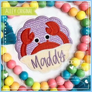 May include: Embroidered applique of a purple and red crab with a white banner that says "Maddy". The crab is surrounded by a colorful beaded garland.