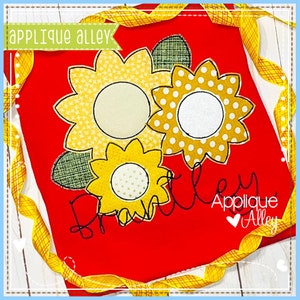 Puede incluir: Tela roja con tres aplicaciones de girasol amarillas y blancas y el nombre "Braxtley" bordado en negro. El texto "Applique Alley" también está bordado en negro con un pequeño corazón.