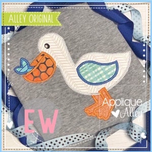 May include: Applique design of a white pelican with orange feet and a blue and white fish in its beak. The design is on a gray fabric with the text "Alley Original" and "Applique Alley" on the fabric.