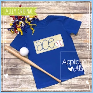 Pode incluir: Uma camiseta azul com a palavra "ace" bordada em um retângulo amarelo com um gráfico de beisebol. A camiseta está sobre uma superfície de madeira com um taco de beisebol e uma bola branca.