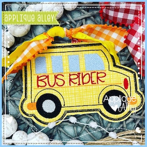 May include: A yellow school bus applique with the text "BUS RIDER" in red. The bus has black wheels and a yellow and orange ribbon attached to the top.