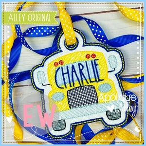 May include: A yellow school bus-shaped tag with the name "CHARLIE" embroidered on the front. The tag is made of felt and has a blue border. It is attached to a yellow and white polka dot ribbon.