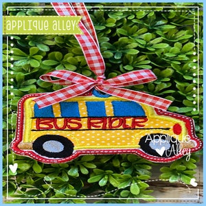 Könnte beinhalten: Gelber Schulbus-Applique mit dem Text "Bus Rider" in Blau und Weiß. Die Applique ist mit gelben Punkten und rotem Besatz verziert. Sie ist an einem rot-weiß karierten Band befestigt.