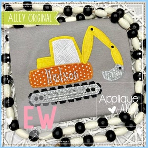 May include: A yellow and gray applique of an excavator with the name "Hudson" on the side. The applique is on a gray shirt with a white and black beaded necklace around it.