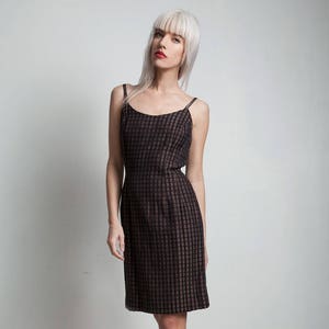 Puede incluir: Una mujer con un vestido de cuadros negros y marrones con tirantes finos. Lleva tacones de plataforma negros con correas.