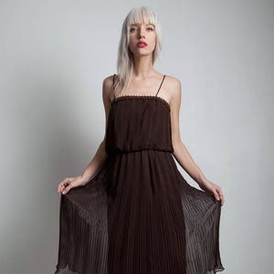 Puede incluir: Un vestido midi plisado marrón con tirantes finos. El vestido está hecho de una tela transparente y tiene un corpiño ajustado. La modelo lleva tacones de plataforma negros.