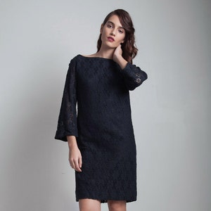 May include: A black lace dress with a boat neck and 3/4 sleeves. The dress is fitted and falls to the knee. The model is wearing nude heels.