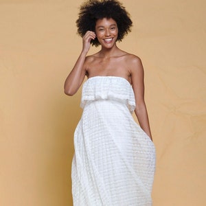 Puede incluir: Una mujer con un vestido blanco de tirantes sin tirantes y un estampado de encaje blanco. Ella sonr&iacute;e y lleva zapatillas blancas.