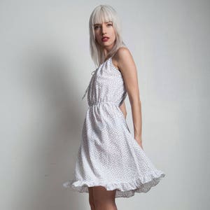 Può includere: Una donna che indossa un abito bianco a fiori con un orlo arricciato e tacchi alti neri.