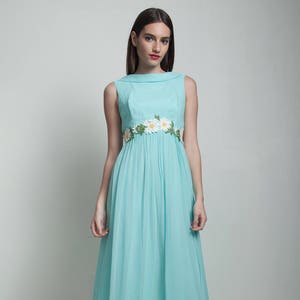 Puede incluir: Un vestido maxi azul claro con un adorno de flores de margarita blancas alrededor de la cintura.