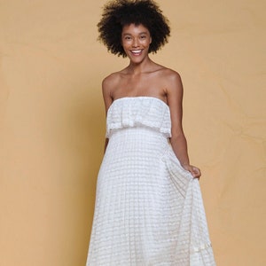 Puede incluir: Un vestido blanco maxi sin tirantes con un patr&oacute;n de encaje y un top con volantes. El vestido tiene una falda de capas y est&aacute; hecho de una tela ligera.
