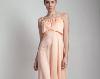 May include: A peach-colored maxi dress with a ruffled neckline and thin straps. The dress has a flowing, A-line silhouette.