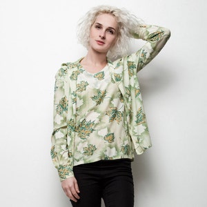 May include: A woman wearing a green and white floral print shirt with black pants and black flats.