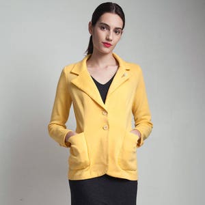 May include: A yellow blazer with a single button closure and two pockets. The blazer is worn over a black v-neck top and a black skirt. The person is wearing black and brown sandals.