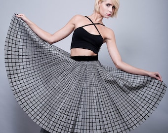 May include: A woman wearing a black crop top and a black and white checkered skirt. She is wearing red heeled sandals and has her hair styled in a short blonde bob.